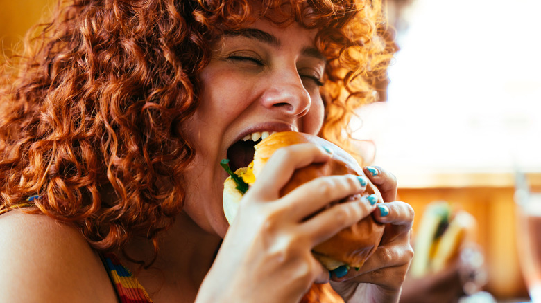 A curly-haired woman biting into a cheeseburger.