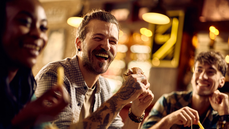 A smiling man eating a burger with friends.
