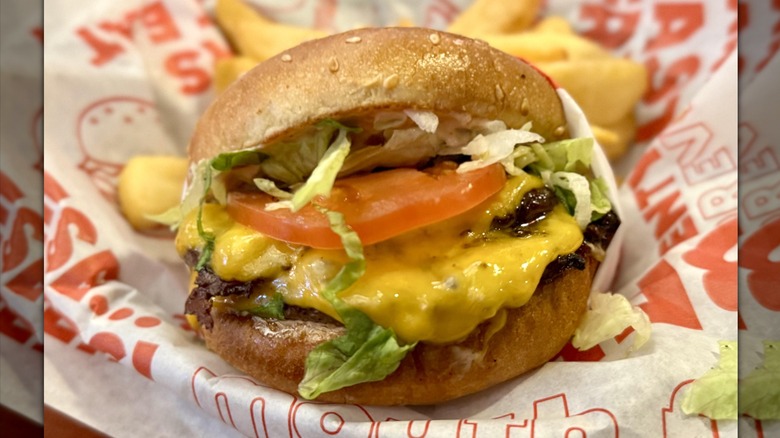 A juicy cheeseburger with tomato and lettuce from Red Robin resting in basket lined with paper.