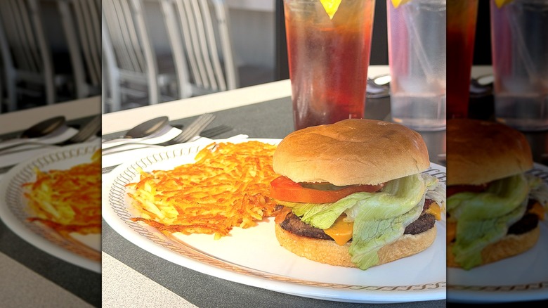 A white plate holding hashbrowns and a cheeseburger with lettuce and tomato at Waffle House.