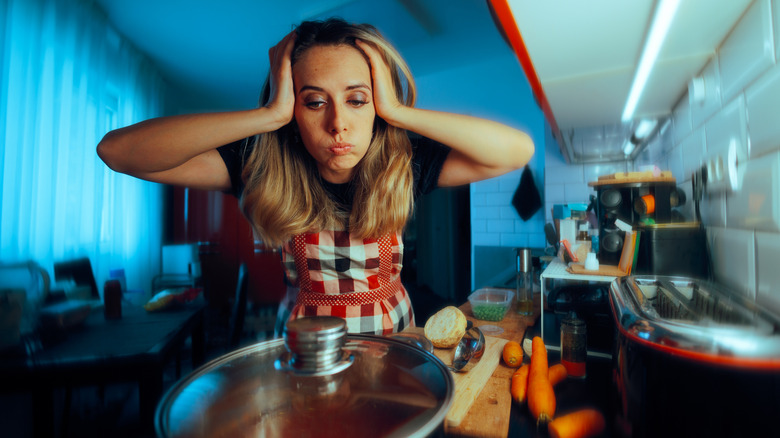 Stressed woman with apron on grabbing hair and looking nervously over the stove