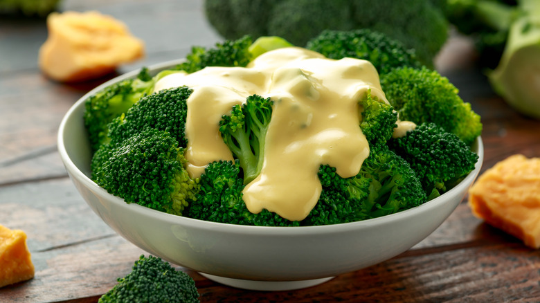 Broccoli with cheese sauce in a white bowl on a wooden table