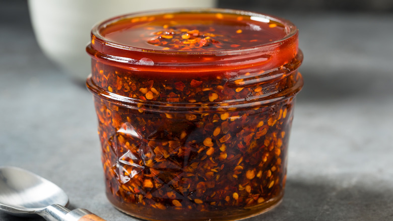 Homemade spicy chili crisp sauce in an open glass jar on a countertop