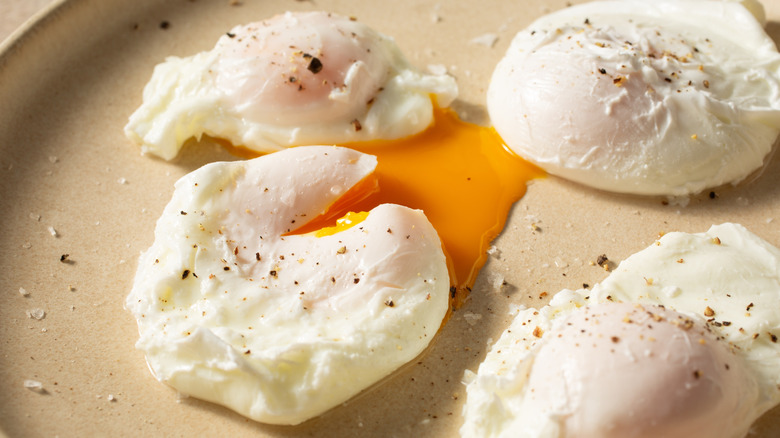 Poached eggs on a pan topped with cracked black pepper, one egg broken so the yolk runs out