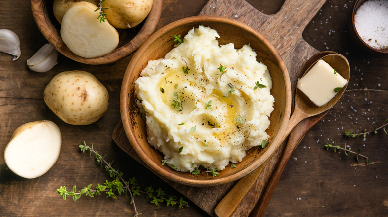 Creamy mushed potatoes with raw potatoes and spices on a rustic background