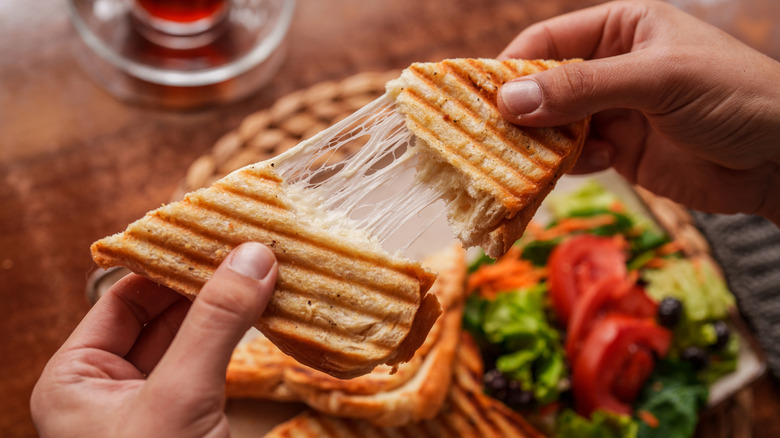 Close-up of a person pulling apart a freshly grilled cheese toast with melted cheese stretching between the slices.