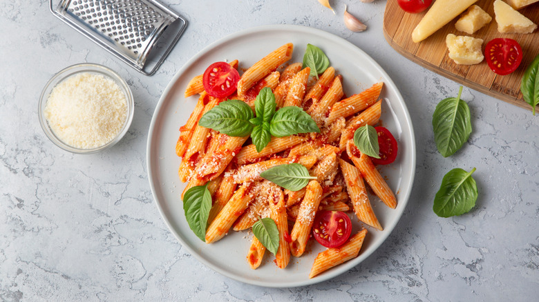 Classic italian pasta penne alla arrabiata with basil and freshly grated parmesan cheese on dark table