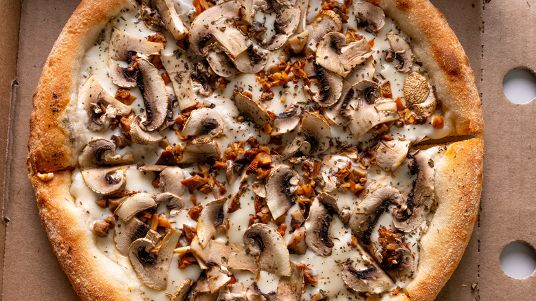 Mushroom pizza with cheese, herbs, and seasonings in a cardboard box