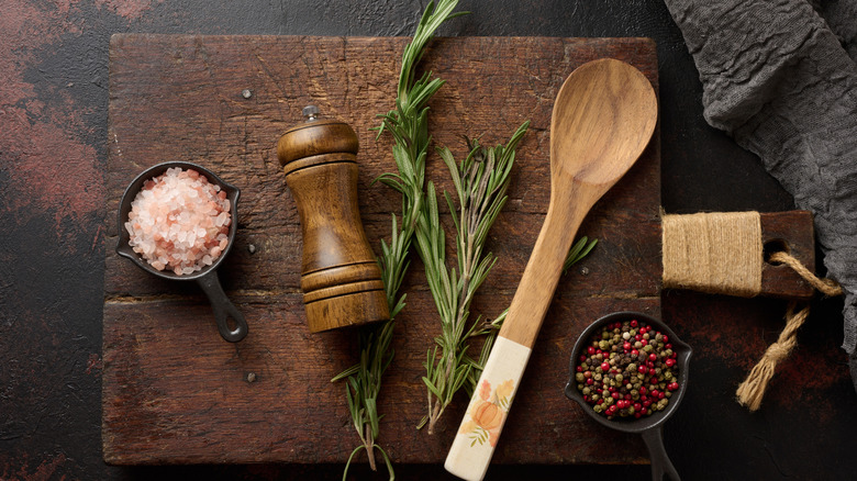 Fresh rosemary, spices and a wood spoon on a board