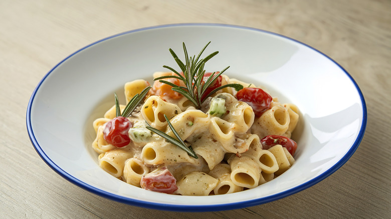 Creamy pasta in a white bowl with fresh rosemary and cherry tomatoes