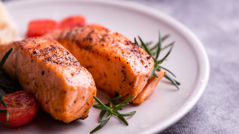 Grilled salmon fillets with black pepper, fresh rosemary, and roasted cherry tomatoes on a white plate.