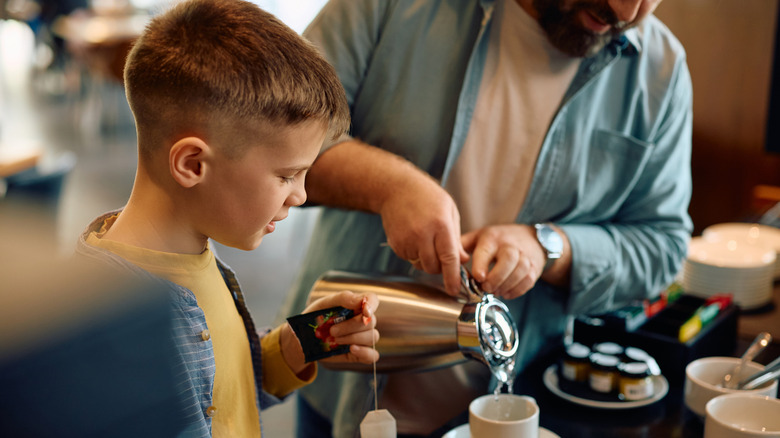 father helping son make tea at buffet