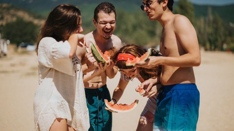 young adults eating watermelon in bathing suits