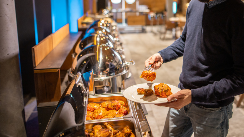 man adding food to plate from buffet