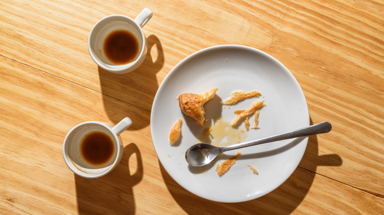 table with plate of bread scraps and empty coffee cups