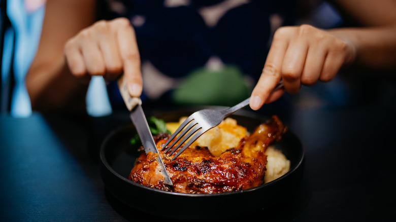 woman cutting chicken with fork and knife