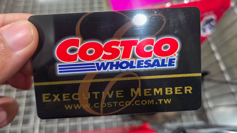 A close up of a Costco executive membership card held up in front of a Costco shopping cart.