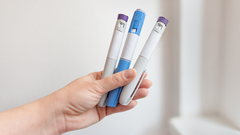A hand holding samples of GLP-1 injection medications.