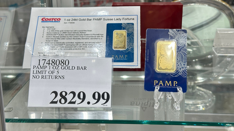 A Costco display behind glass of a 1 ounce engraved gold bar from Pamp brand priced $2829.99