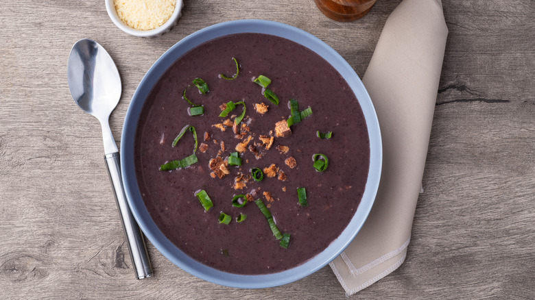 Black bean soup with napkin, spoon, and side of grated cheese