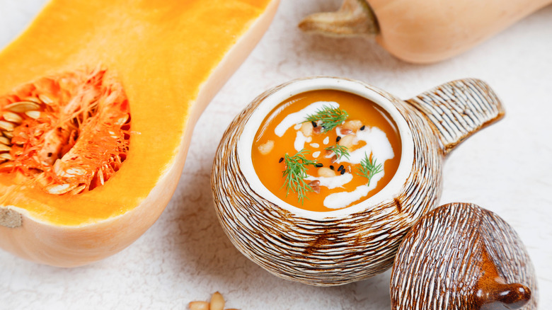 Raw butternut squash cut in half next to butternut squash soup in festive, decorative bowl
