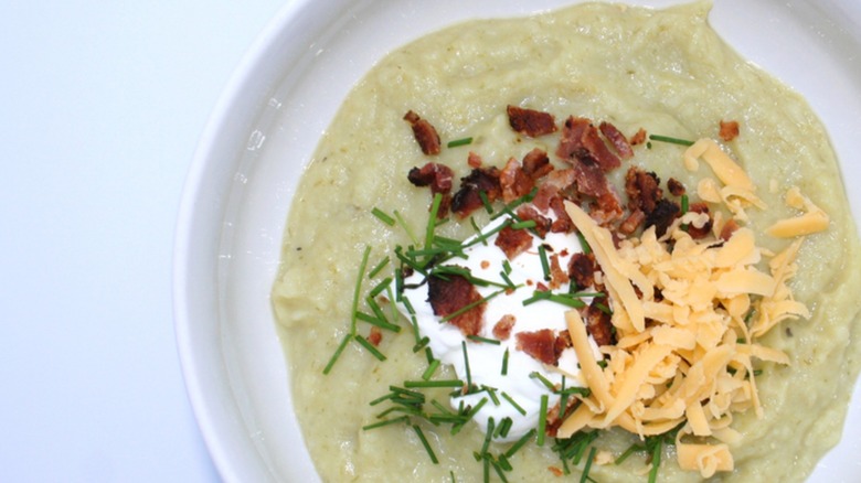 Bowl of baked potato leek soup garnished with bacon crumbles, shredded cheese, chives, and sour cream