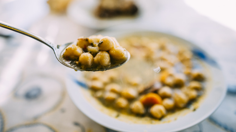Spoon holding chickpeas over bowl of soup