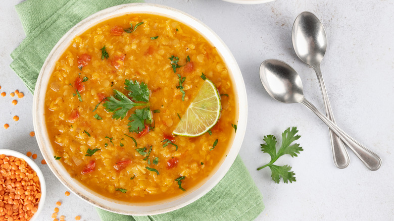 Bowl of red lentil soup topped with cilantro and lime wedge on green dish towel
