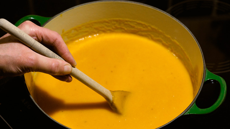 Hand stirring carrot soup with wooden spoon in green enamel pot