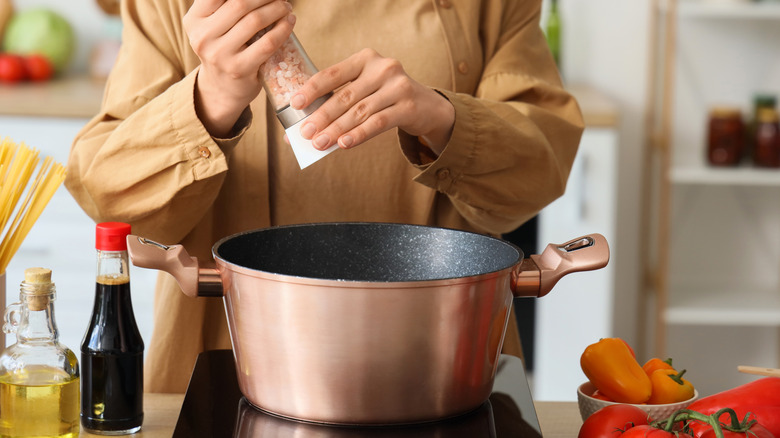 Woman cooking and grinding salt into soup pot in kitchen