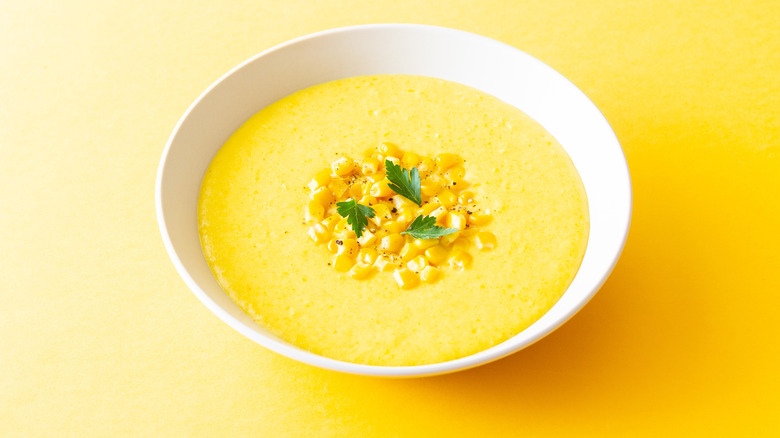 Bowl of corn soup topped with fresh corn and herbs on yellow background