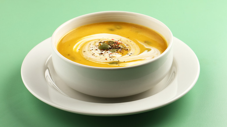 Pumpkin soup in white bowl on green background