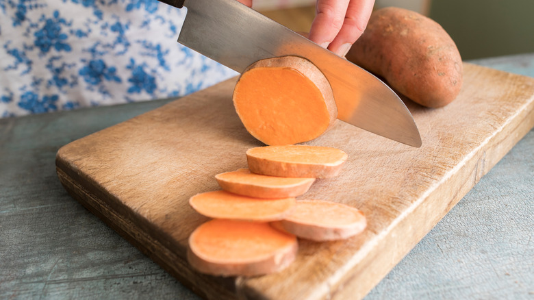 woman chopping sweet potatoes on wooden board