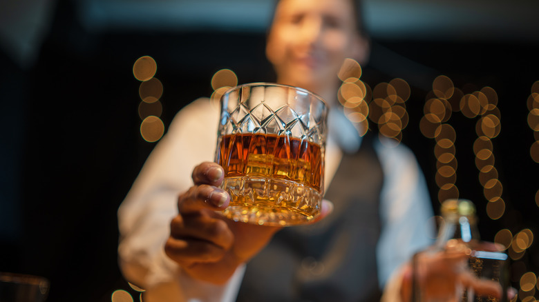 Person handing a whiskey glass toward the camera