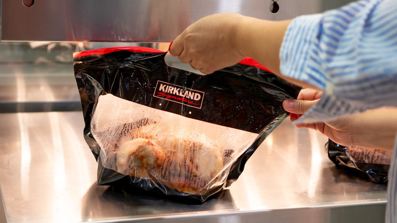 Hand lifts rotisserie chicken bag from Costco's hot food section
