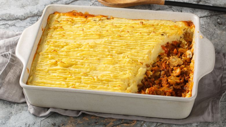 Shepherd's pie in casserole dish on top of towel next to a wooden spoon