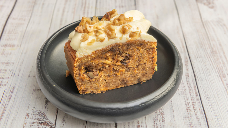 Spice cake with frosting topped with walnuts on small black plate