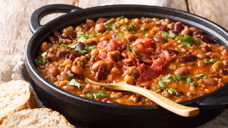 Calico beans sprinkled with fresh parsley in a cast iron bowl with wooden spoon