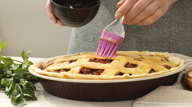 Woman brushing egg wash over lattice bean pie crust