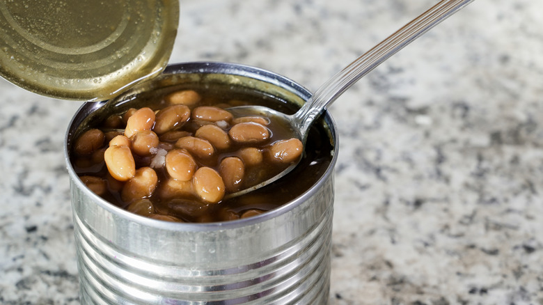 Opened can of baked beans with a spoon scooping a serving out of it