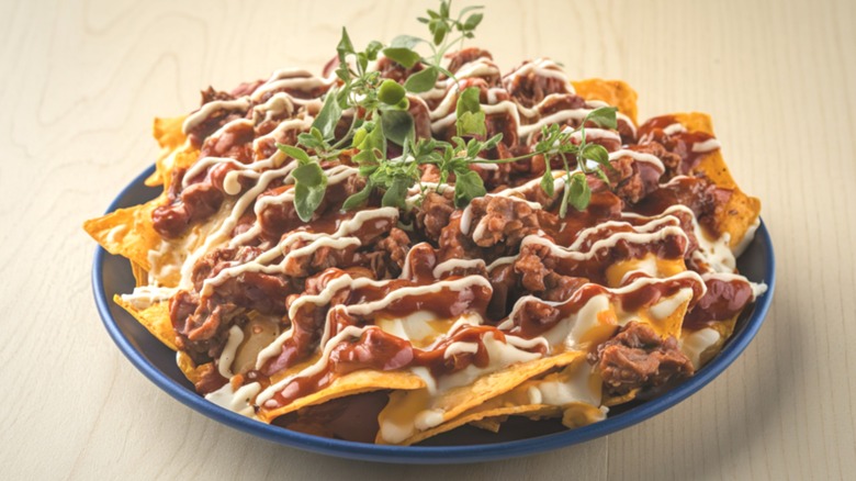 Nachos with beans and other toppings served with garnish on blue plate