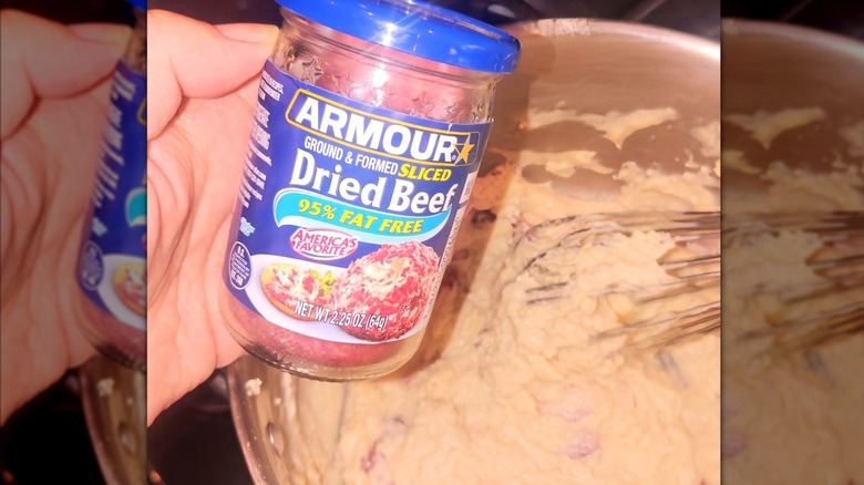 Someone holding a can of dried beef above a full mixing bowl.