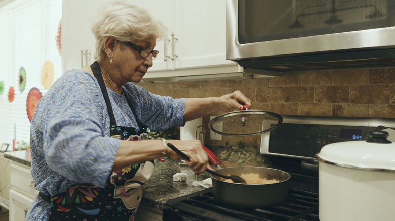 A senior woman preparing a dish on the stove.