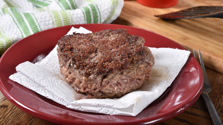 A large meat patty and a grease-splattered napkin on a red plate.