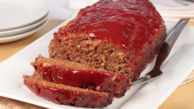 A partially sliced meatloaf on a white plate.