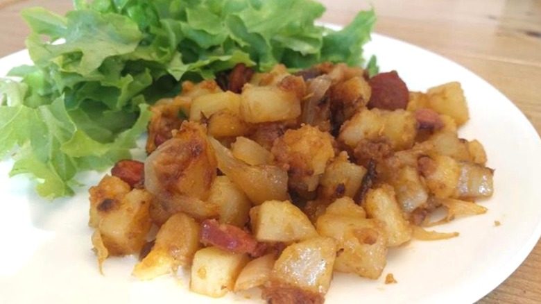 A plate of chopped lettuce, potatoes, hot dogs, and onions.
