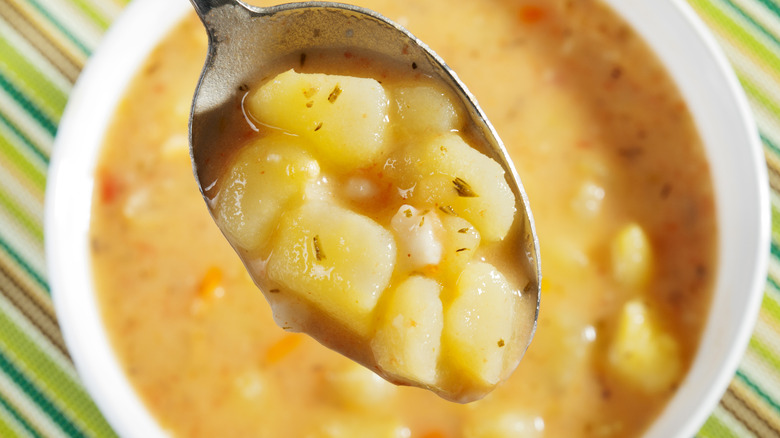 Someone holding a spoonful of potato soup above the bowl.