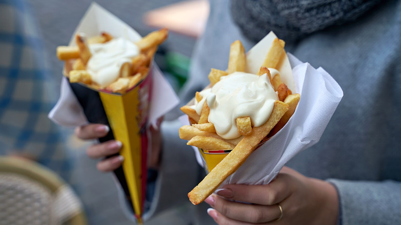 Person holds two Belgian frites loaded with mayonnaise