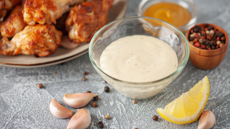 Ramekin of Alabama white sauce next to lemon wedge, peppercorns, garlic, vinegar, and chicken
