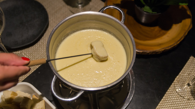 Hand dipping bread into fondue pot of melted cheese